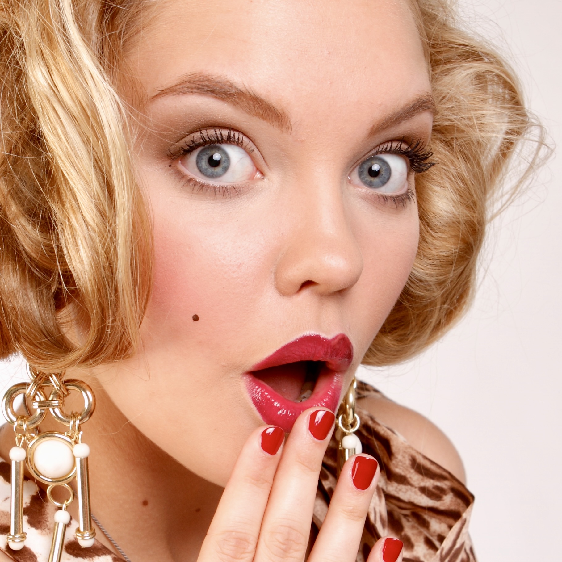 model in makeup with red lips and matiching nails. posed with hand infront of open mouth looking shocked or suprised
